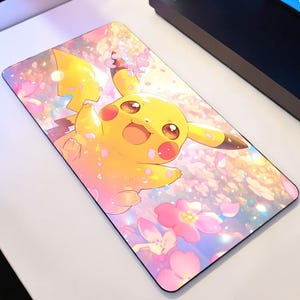 May include: A rectangular mousepad featuring a yellow Pikachu character with a cheerful expression, set against a backdrop of pink cherry blossoms. The design has a soft, pastel color palette, with a black border.