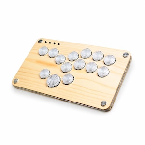 May include: A rectangular arcade controller featuring a light-colored wooden top panel with a natural grain pattern. It includes twelve circular, translucent, ridged buttons arranged in a layout, along with four small black buttons and metal fasteners.