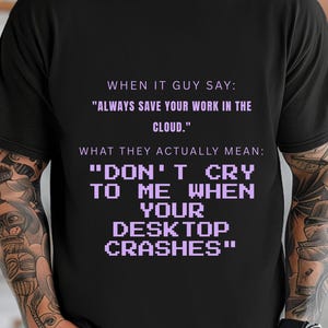 May include: A black short-sleeved t-shirt featuring light purple text that reads: WHEN IT GUY SAY: "ALWAYS SAVE YOUR WORK IN THE CLOUD." WHAT THEY ACTUALLY MEAN: "DON'T CRY TO ME WHEN YOUR DESKTOP CRASHES" with the second part in a pixelated font.