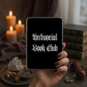Könnte beinhalten: Eine rechteckige schwarze Tablet-Hülle mit dem weißen Schriftzug Antisocial Book Club in einer gotischen Schriftart. Die Hülle hat einen transparenten Rand und wird aufrecht gehalten, wobei die Schrift deutlich auf dem schwarzen Grund zu sehen ist.