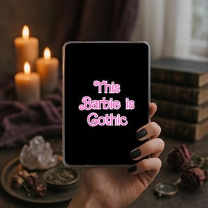 May include: A rectangular black tablet or phone case featuring the pink text This Barbie is Gothic in a retro-style font. The text is centered on the black surface, which has a clear border around the edges, presenting a bold and high-contrast design.
