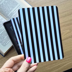 May include: A rectangular card featuring a vertical striped pattern in alternating black and light blue colours. The card has rounded corners and a smooth, flat surface. It is positioned in front of an open book with visible printed text.