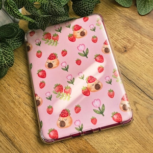 May include: A clear protective tablet case featuring a repeating pattern on a light pink background. The design includes illustrations of small brown animals wearing strawberry hats, red strawberries with green leaves, and pink tulip flowers.