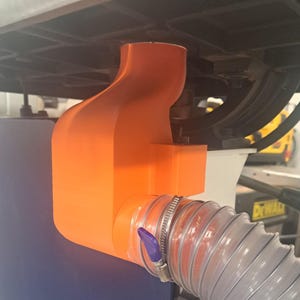May include: An orange 3D-printed dust collection port attached to a blue and white band saw. A clear, flexible hose is connected to the port with a metal clamp. The band saw is labeled "14" 10-326".