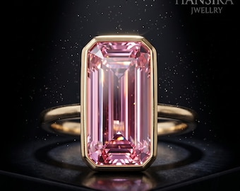 May include: A gold ring featuring a large, rectangular, pink gemstone. The gemstone is set in a gold bezel and has a step-cut design. The ring is displayed against a dark background with the text "HANSIKA JWELLRY".
