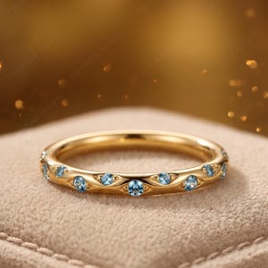 Könnte beinhalten: Ein goldener Ring mit einer Reihe kleiner, runder, hellblauer Edelsteine, die in einzelne marquiseförmige Metallfassungen eingefasst sind, welche den gesamten Umfang des Rings umschließen und ein strukturiertes, sich wiederholendes Muster bilden.