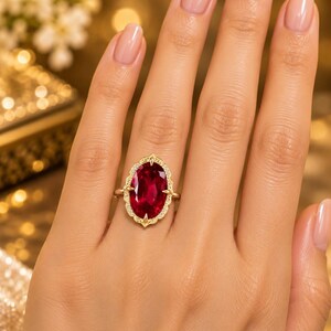 K&ouml;nnte beinhalten: Ein Goldring mit einem gro&szlig;en, oval geschliffenen, tiefroten Edelstein als Herzst&uuml;ck. Der Stein ist von einer dekorativen, gewellten Goldfassung mit feinen Details und kleinen, eingelassenen Akzentsteinen am &auml;u&szlig;eren Rand umgeben.