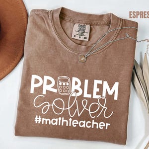 Op de afbeelding: Een witte keramische mok met een zwarte handgreep en de tekst "But First, Coffee" in een handschriftstijl. De mok staat op een wit oppervlak. De mok is ongeveer 10 cm hoog.