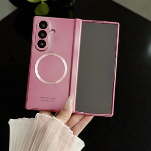 May include: Pink foldable phone case with a triple-lens camera and a circular design element. The case is open, revealing the phone's screen. The text "FOLD CASE DESIGN BY ZLS" is printed on the case.
