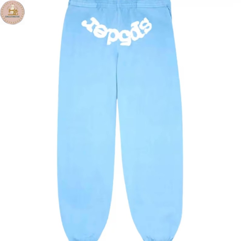 Puede incluir: Pantalones de ch&aacute;ndal azul claro con la palabra "spider" en blanco, arqueada en la parte trasera de la cintura. Los pantalones son de color liso, con un corte holgado y cintura con cord&oacute;n. La tela parece suave y c&oacute;moda.