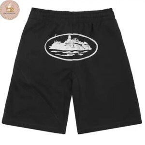 May include: Black shorts featuring an elastic waistband and a white graphic print centered on the upper portion. The graphic depicts a detailed illustration of a large ship enclosed within a white oval border, set against the solid black fabric.