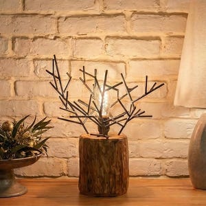 Puede incluir: Escena de decoración rústica con una mesa de madera frente a una pared de ladrillo. La mesa exhibe un arreglo floral decorativo, una lámpara con forma de rama de árbol y una lámpara de piedra con pantalla de lino.