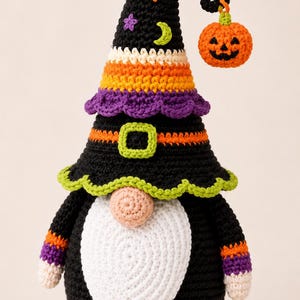 May include: A crocheted gnome figure wearing a black pointed hat decorated with orange, purple, and yellow stripes, small stars, and a crescent moon. A small orange jack-o'-lantern hangs from the hat tip. The gnome has a white beard and nose.