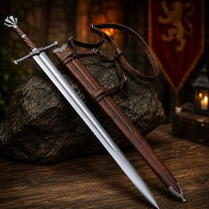 Puede incluir: Una espada de acero con empuñadura marrón trenzada y guarda plateada, acompañada de una vaina de cuero marrón a juego con correas integradas. La hoja es larga, puntiaguda y metálica, descansando junto a la funda sobre una superficie oscura.