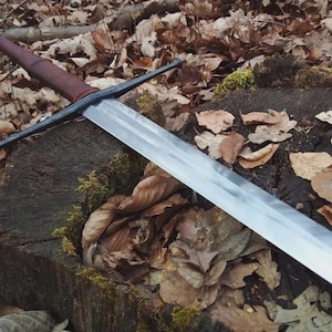 May include: A longsword with a polished steel blade, a dark brown leather-wrapped grip, and a black metal crossguard. The sword features a pommel at the end of the handle and a straight, double-edged blade that tapers towards the pointed tip.