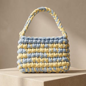 Könnte beinhalten: Eine kleine, handgefertigte Tragetasche in einem gewebten Design. Die Tasche hat abwechselnd horizontale Streifen in Hellblau und Gelb. Der Griff ist ein geflochtenes Design in passenden Farben. Die Tasche steht auf einer hellbraunen Oberfläche.