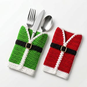 May include: Two crochet cutlery holders shaped like holiday outfits. One is green with a black belt and gold buckle, holding a silver fork, knife, and spoon. The other is red with a black belt and gold buckle, featuring white trim.