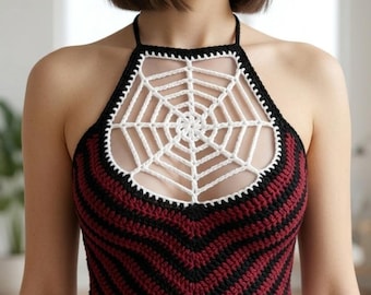 May include: A halter-style crochet crop top featuring a white spiderweb pattern across the chest and a chevron-striped design in alternating black and deep red yarn. The garment has thin black straps and a straight hemline at the waist.