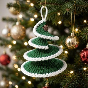 May include: A spiral-shaped Christmas tree ornament crocheted from dark green yarn with white yarn edging along the tiers. The ornament features a small brown crocheted accent at the top and a white yarn loop for hanging on a tree branch.