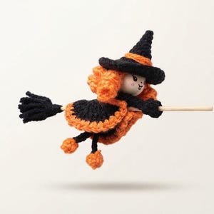 May include: A crocheted witch doll with orange hair and a black pointed hat, wearing a black and orange dress. The doll is attached to a wooden broomstick handle with a black yarn broom head, featuring a small wooden face with painted features.