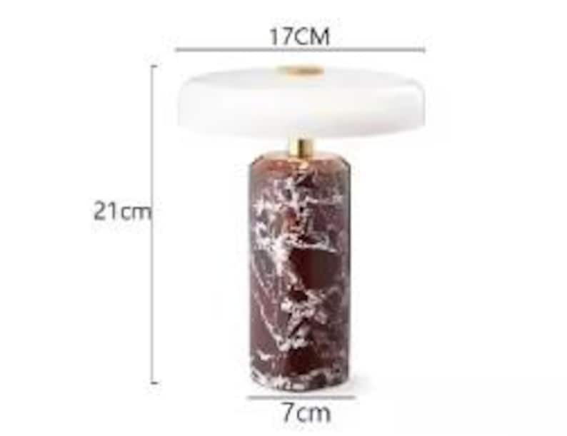 May include: A decorative table lamp with a white lampshade and a cylindrical base. The base is a dark red color with white marbling. The lamp is 21 cm tall, the lampshade is 17 cm wide, and the base is 7 cm wide.