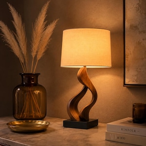 Peut inclure: Une lampe de table avec un abat-jour cylindrique en tissu beige et une base en bois sculptée et torsadée reposant sur un socle carré noir. La lampe émet une lueur chaude et douce, éclairant les environs d'une lumière ambiante apaisante.