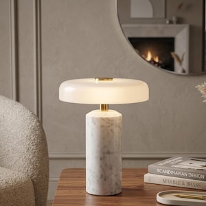 Peut inclure: Une lampe de table moderne avec un abat-jour blanc arrondi et un socle en marbre. La lampe a un accent doré et est posée sur une table en bois. La lampe est allumée, émettant une douce lueur. La lampe fait partie d'une collection de décoration intérieure.