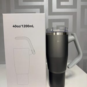 May include: A dark grey insulated tumbler with a grey handle and a clear lid. The tumbler is next to a white box with the text "40oz/1200mL" and a line drawing of the tumbler with a straw.