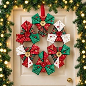 May include: A circular fabric wreath composed of six folded triangular segments in red, green, and white patterns. Each segment is accented with a central button and smaller buttons. The wreath is suspended by a red ribbon loop on a door.
