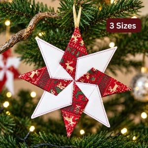 May include: A fabric star ornament featuring alternating points of solid white and red fabric with a gold reindeer and tree pattern. The star is suspended by a gold ribbon loop and includes a text overlay in the corner that reads 3 Sizes.