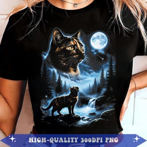 May include: A black short-sleeved t-shirt featuring a graphic print of a tortoiseshell cat looking up at a full moon above a forest landscape with a waterfall and a smaller cat standing on a rock in the foreground, with text at the bottom.