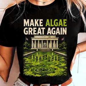 Könnte beinhalten: Ein schwarzes T-Shirt mit dem Text MAKE ALGAE GREAT AGAIN in weißer und grüner Schrift. Unter dem Text befindet sich eine grafische Illustration des Lincoln Memorials mit einem leuchtend grünen, algengefüllten Teich im Vordergrund.