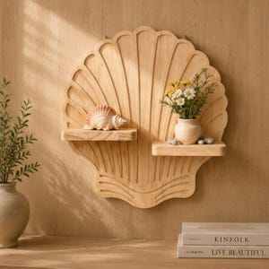May include: A light-colored wooden wall shelf shaped like a large scallop shell with two horizontal tiers. The left shelf holds a single seashell, while the right shelf displays a small ceramic vase containing white and yellow flowers with green stems.