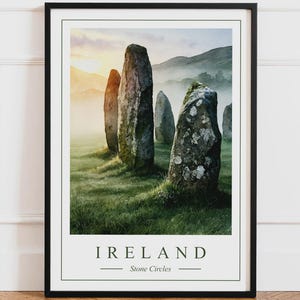 Peut inclure: Une impression d'art encadrée représentant un paysage de hautes pierres levées patinées dans un champ herbeux lors d'un lever de soleil brumeux. Le texte IRELAND et Stone Circles est imprimé en vert foncé au bas de l'image à bordure blanche.