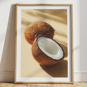 Peut inclure: Impression encadrée avec deux noix de coco, une entière et une coupée, révélant la chair blanche. Les noix de coco ont des extérieurs bruns et fibreux. Le fond est jaune clair avec des ombres, et le cadre est brun clair.