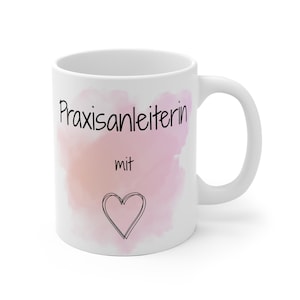 Può includere: Tazza in ceramica bianca con le parole "Praxisanleiterin mit" in nero, uno sfondo rosa e pesca in stile acquerello e un contorno a forma di cuore nero. La tazza ha un manico curvo.