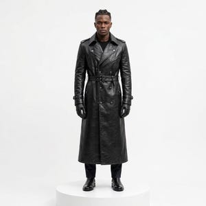 May include: A long black leather trench coat featuring a double-breasted front, a wide notched collar, shoulder epaulets, and a matching waist belt with a buckle. The coat includes long sleeves with buckled cuffs and is worn with black leather gloves.