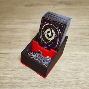 Peut inclure: Un boîtier de rangement pour cartes noir et rouge contenant un jeu de cartes avec un emblème d'étoile dorée au dos et une collection de petits jetons de jeu circulaires avec des valeurs numériques imprimées, le tout dans un compartiment.