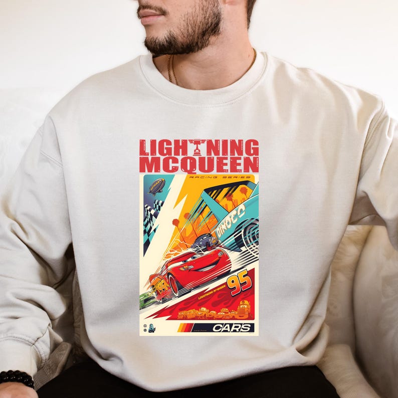 May include: Cream-colored sweatshirt featuring a graphic of Lightning McQueen from the Cars movie. The design includes the text "LIGHTNING McQUEEN" in red, with racing cars and the number "95". The Cars logo is at the bottom.