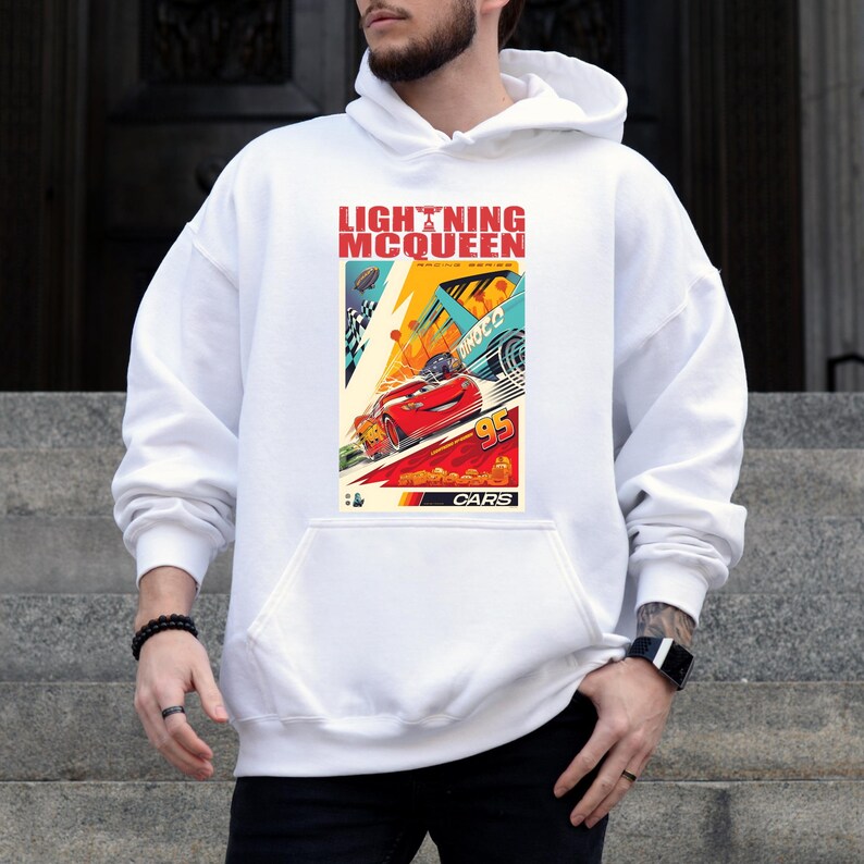 May include: White hoodie featuring a colorful graphic of Lightning McQueen from the movie Cars. The graphic includes the text "LIGHTNING MCQUEEN RACING WORLD" and the number "95". The hoodie has a front pocket and a drawstring hood.