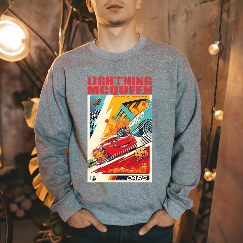 May include: Gray crewneck sweatshirt featuring a colorful graphic of Lightning McQueen from the Cars movie. The graphic includes the text "LIGHTNING MCQUEEN RACING SERIES" and the number "95". The word "CARS" is also visible.