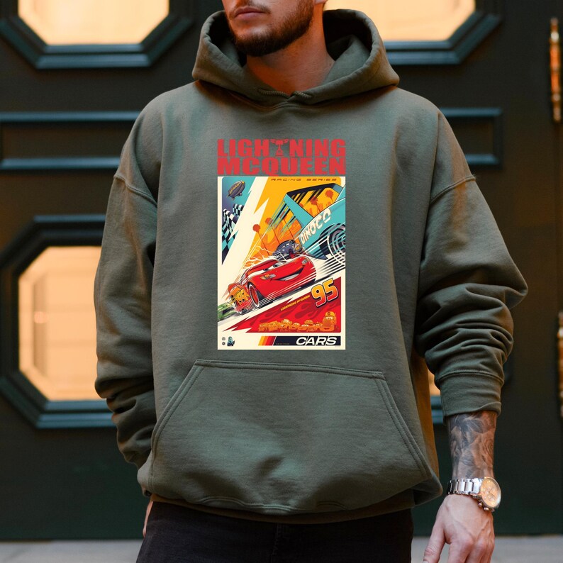 May include: An olive green hoodie featuring a graphic from the movie Cars. The graphic includes the text "LIGHTNING McQUEEN RACING SERIES" and a red race car with the number 95. The hoodie has a front pocket and a hood.
