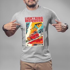 May include: A gray t-shirt featuring a colorful graphic of Lightning McQueen from the Cars movie. The graphic includes the text "LIGHTNING McQUEEN RACING SERIES" and the number "95". The design showcases a red race car in action.