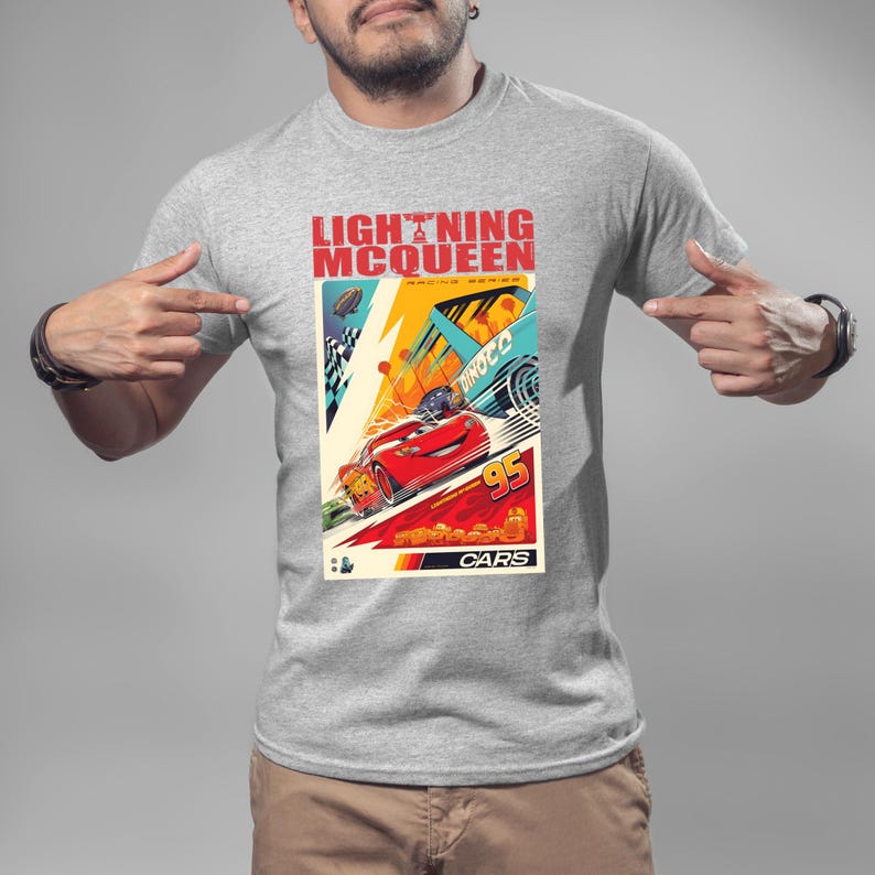May include: A gray t-shirt featuring a colorful graphic of Lightning McQueen from the Cars movie. The graphic includes the text "LIGHTNING McQUEEN RACING SERIES" and the number "95". The design showcases a red race car in action.