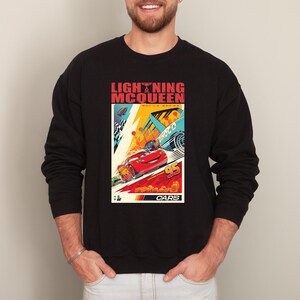 May include: Black sweatshirt featuring a colorful graphic of Lightning McQueen from the movie Cars. The design includes the text "LIGHTNING MCQUEEN" and "95". The graphic has a retro, vintage style with vibrant colors.