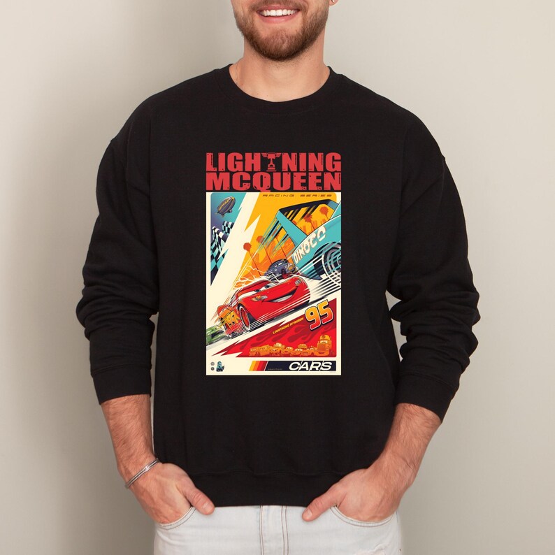 May include: Black sweatshirt featuring a colorful graphic of Lightning McQueen from the movie Cars. The design includes the text "LIGHTNING MCQUEEN" and "95". The graphic has a retro, vintage style with vibrant colors.