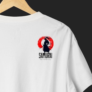 Op de afbeelding: Wit T-shirt met een zwart silhouet van een samoerai krijger in een rode cirkel. Het woord "SAMURAI" is in het zwart onder de afbeelding gedrukt, met Japanse tekst eronder.