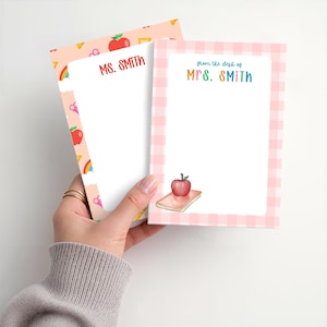 May include: Two rectangular notepads with white centers. The left notepad has a peach background with school-themed icons and the red text MS. SMITH. The right notepad has a pink gingham border, the text from the desk of MRS. SMITH, and an apple on a book.