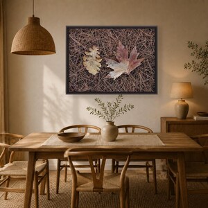 May include: A rectangular framed wall art piece featuring a high-resolution photograph of two fallen leaves, one oak and one maple, resting on a dense bed of brown pine needles. The artwork is displayed in a dark frame on a neutral-toned wall.