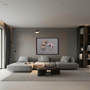 May include: A rectangular framed wall art piece featuring a close-up of three dried brown seed pods and a curved pinkish-white dried plant stem, displayed on a textured grey background, mounted on a solid grey wall above a grey modular sofa.